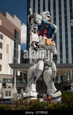 Vista verticale ad angolo basso di una donna che passa dall'enorme e impressionante statua unicorno Gundam a grandezza naturale in Divercity Tokyo Plaza, Odaiba Island, Tokyo Foto Stock