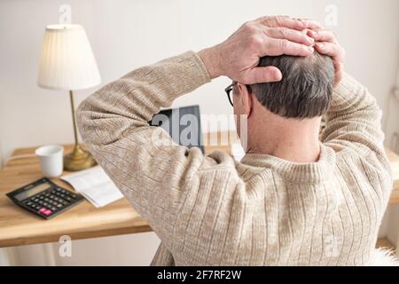 L'uomo anziano ha preoccupato circa le fatture che si siedono a casa tenendo le mani sulla testa che è stressato con i debiti. Foto Stock