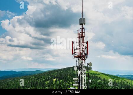 Torretta trasmettitore per telecomunicazioni con antenne di comunicazione cellulare in montagna contro cielo e nuvole Foto Stock