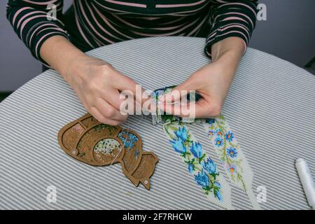 Tessitura da perle. Primo piano - le mani di una donna sono perline a nastro su un filo, facendo gioielli. La donna è affettuosa di tessitura dalle perle. Foto Stock