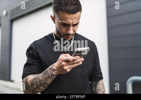 Uomo spagnolo con tatuaggi guardando il suo telefono con un volto preoccupato Foto Stock