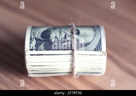 I dollari STATUNITENSI si sono arrotolati e stretti con la fascia isolata tavolo di legno Foto Stock