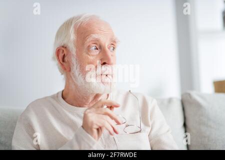 Foto di uomo anziano pensionato sedersi casa divano interno grave pensa sognare sognare guardare spazio vuoto Foto Stock