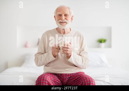 Foto di anziano uomo pensionato siedono cattiva casa felice positivo sorrisi godetevi una tazza di tè indossare pigiami Foto Stock