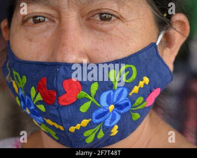 La donna messicana indossa una maschera colorata in tessuto ricamato e lavabile e guarda la fotocamera durante la pandemia mondiale del coronavirus. Foto Stock