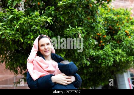 giovane donna adulta con sciarpa rosa sulla testa contro il cancro che porta il suo bambino di sei mesi. concetto di maternità e cancro Foto Stock