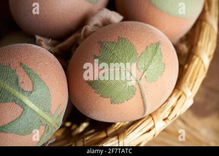 Uova di Pasqua crude con foglie di piante fresche attaccate con calze, pronte per essere tinte con bucce di cipolla Foto Stock