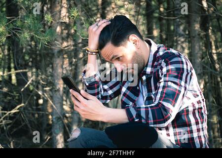 Closeup di un uomo lumberjack che pettina i capelli e utilizza un smartphone mentre si riposa nella foresta Foto Stock