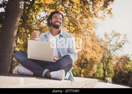 Ritratto di bel ragazzo allegro viaggio blogger seduta cemento bere latte utilizzando il computer portatile soleggiato giorno all'aperto Foto Stock