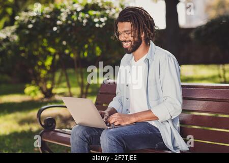 Ritratto fotografico dell'uomo in occhiali che lavora sul computer facendo progetto seduto sulla panchina nel parco sorridente Foto Stock