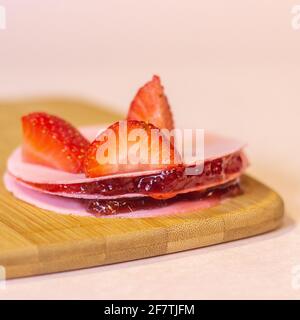 Closeup di wafer ripieni di confettura di fragole e fresco pezzi di fragola su una tavola di legno Foto Stock