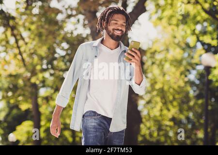 Ritratto di simpatico ragazzo allegro che usa il dispositivo che chiacchiera passatempo passeggiando aria fresca all'aperto Foto Stock