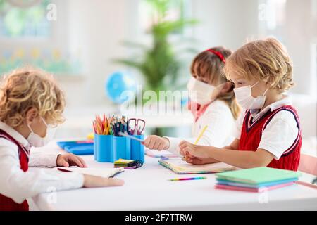 Bambini in maschera facciale in classe scolastica. Il bambino torna a scuola dopo il blocco del coronavirus. Bambino primario nella pandemia di covid-19. Foto Stock