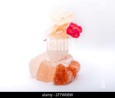 Grandi pezzi di sale marino dell'Himalaya e di un fiore rosso del deserto sono impilati uno sull'altro per la pace e l'equilibrio. Isolato su uno sfondo bianco Foto Stock