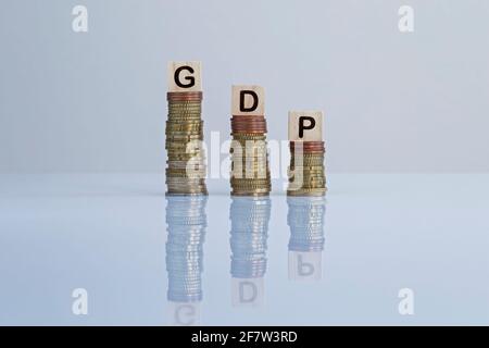 Parola 'PIL' sui blocchi di legno in cima a pile discendenti di monete. Foto concettuale del PIL (prodotto interno lordo) indicatore economico, economia e recessione. Foto Stock