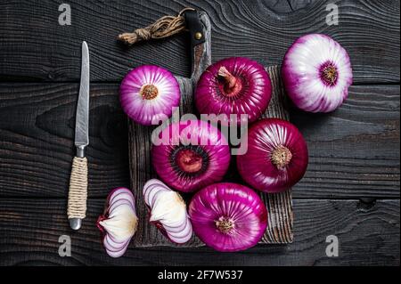 Cipolla dolce rossa intera e halfed piatta su un tagliere. Sfondo di legno nero. Vista dall'alto Foto Stock