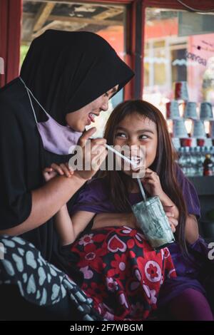 MANINJAU, INDONESIA - 12 febbraio 2021: Bevanda di condivisione tra mamma e figlia. Grande complicità Foto Stock