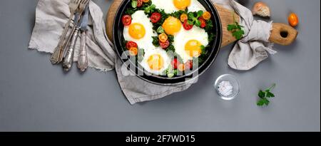 Uova fritte con spinaci e pomodori ciliegini con caffè sul lato per la colazione. Sfondo grigio. Vista dall'alto, spazio di copia, banner panoramico Foto Stock