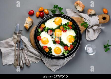 Uova fritte con spinaci e pomodori ciliegini con caffè sul lato per la colazione. Sfondo grigio. Vista dall'alto Foto Stock