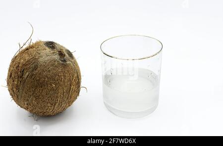 Foto isolata di una noce di cocco e accanto ad essa un bicchiere d'acqua di cocco su sfondo bianco Foto Stock