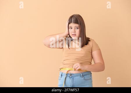 Scioccata ragazza sovrappeso che misura la sua vita su sfondo a colori Foto Stock