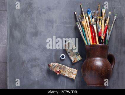 Vecchio pennello e tubi sulla texture astratta di sfondo della tabella. Concetto e strumenti di pittura d'arte Foto Stock