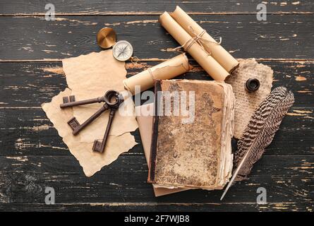 Composizione con libro antico, piuma, bussola, scroll e tasti su sfondo di legno scuro Foto Stock