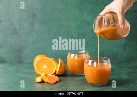 Donna che versa il frullato dal vaso in vetro su sfondo colorato Foto Stock