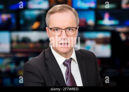 Un anchorman che riporta notizie dal vivo in studio TV. Sfondo di più schermi della sala di controllo delle trasmissioni. Concetto di giornalismo Foto Stock