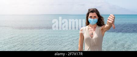 Banner orizzontale o testata Ritratto di giovane donna che indossa una maschera protettiva che mostra il pollice verso il basso. Splendido sfondo con acqua blu chiara. Foto Stock