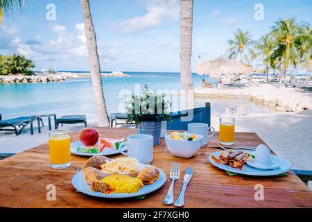 Prima colazione su un tavolo vicino alla spiaggia che si affaccia sull'oceano, mare caraibico con tavolo per la colazione con caffè succo d'arancia, croissant e frutta Foto Stock