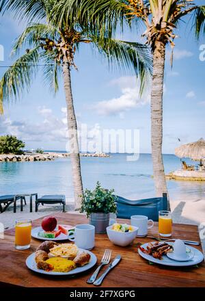 Prima colazione su un tavolo vicino alla spiaggia che si affaccia sull'oceano, mare caraibico con tavolo per la colazione con caffè succo d'arancia, croissant e frutta Foto Stock