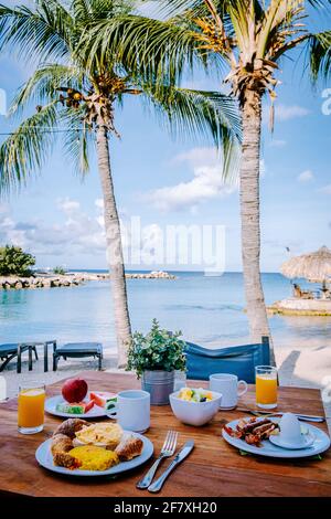 Prima colazione su un tavolo vicino alla spiaggia che si affaccia sull'oceano, mare caraibico con tavolo per la colazione con caffè succo d'arancia, croissant e frutta Foto Stock