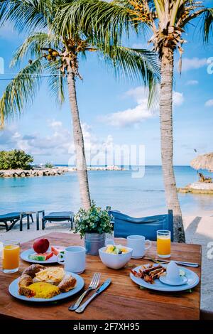 Prima colazione su un tavolo vicino alla spiaggia che si affaccia sull'oceano, mare caraibico con tavolo per la colazione con caffè succo d'arancia, croissant e frutta Foto Stock