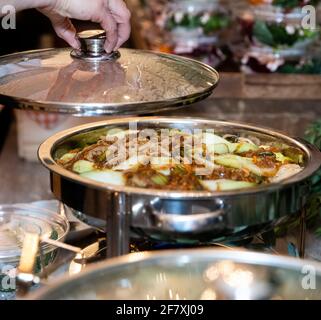 ricetta asiatica in un piatto di metallo su un buffet tavolo con una mano che solleva il coperchio Foto Stock