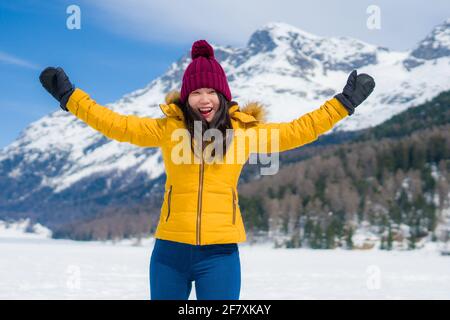 Giovane donna cinese asiatica felice e allegra in giacca invernale e cappello che corre divertente su lago ghiacciato coperto di neve Sulle Alpi svizzere godendo Foto Stock