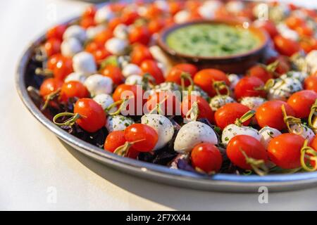 Pomodori ciliegini e palle di formaggio su un bastone presentato sopra una piastra rotonda in metallo con salsa al centro Foto Stock