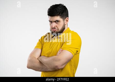 Uomo arrabbiato offeso che tiene le braccia incrociate e fissando la macchina fotografica con lo sguardo scettico e diffidente, ritenendosi pazzo a qualcuno. Espressioni facciali umane Foto Stock