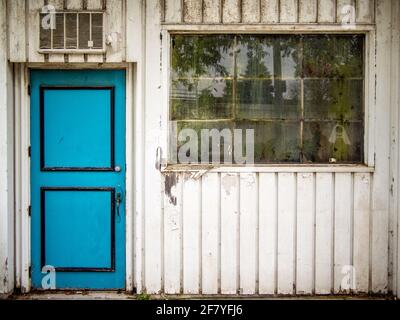 Porta turchese su un muro con una finestra rotta la facciata di una casa abbandonata Foto Stock