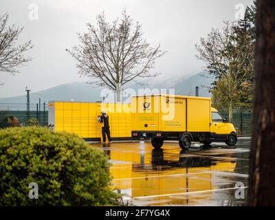 Lahnstein, Germania, 10. Aprile 2021: Un dipendente del gruppo 'Deutsche Post DHL Group' consegna pacchi e pacchetti a una stazione di imballaggio con un veicolo elettrico Foto Stock