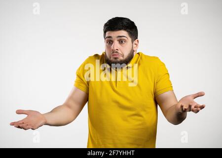 Indifferente uomo incerto fa gesto di non so, cant aiutare qualsiasi cosa. Concetto di domanda difficile. Ragazzo con barba su sfondo bianco studio. Foto Stock