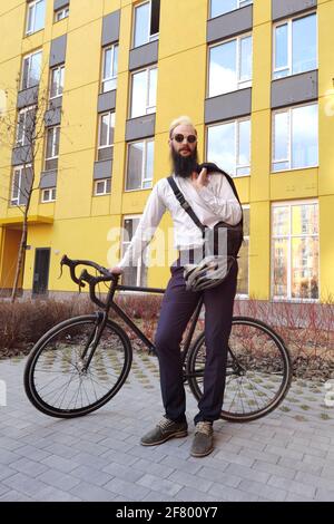 Un giovane uomo d'affari alla moda che spinge una bicicletta mentre va a lavorare. Foto Stock