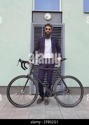 Un giovane uomo d'affari alla moda che spinge una bicicletta mentre va a lavorare. Foto Stock