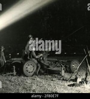 Soldati KNIL operativi, supportati da un proiettore, una pistola Bofors 40 mm durante un esercizio notturno. Foto Stock