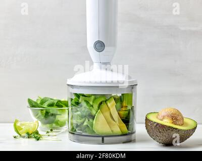 avocado, sedano e spinaci in contenitore trasparente in plastica per preparare un sano frullato da colazione sul tavolo da cucina Foto Stock