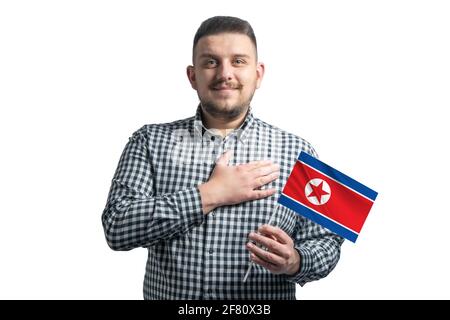 Ragazzo bianco che tiene una bandiera della Corea del Nord e tiene la mano sul suo cuore isolato su uno sfondo bianco con amore per la Corea del Nord. Foto Stock