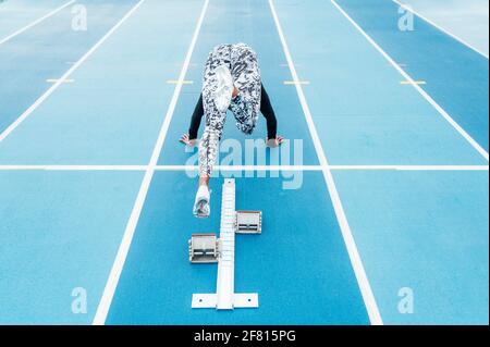 Vista posteriore di giovane forte sportivo che comincia a correre veloce dai blocchi di partenza durante la pista e l'allenamento sul campo allo stadio Foto Stock