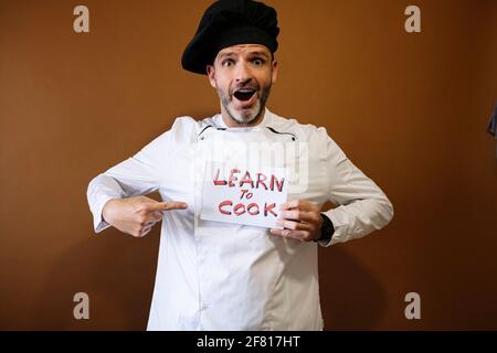 Chef uomo con un segno che dice imparare e cucinare Foto Stock