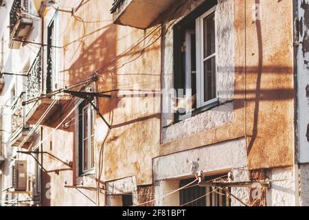 Vista di un muro intonacato arancione di un'antica casa residenziale con finestre multiple, un sacco di corde di essiccazione che si estendono tra, e un animale domestico - Foto Stock