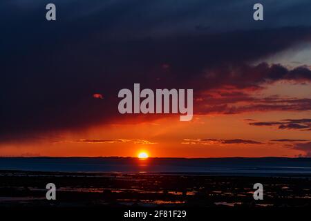 Morecambr Bay, Lancashire, Regno Unito. 10 Apr 2021. Il sole tramonta attraverso la baia di Morecambe tra Barrow e le nubi della tempesta di avvicinamento Credit: PN News/Alamy Live News Foto Stock